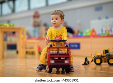 One Year Old Boy Dressed In Yellow Driving A Toy Fire Truck At A Kids Playground