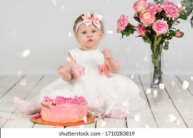 One year old child with a birthday cake. Funny little girl smeared with cream on her birthday. Funny child on holiday. Cute baby girl with pink pastries is sitting on the floor.