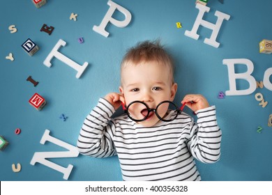 One year old child lying with spectacles and letters on blue background