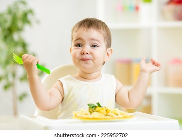 One Year Old Kid Boy In A Highchair For Feeding With A Fork And A Plate In The Kitchen