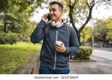 One young adult caucasian man walking in the city town near park using mobile phone smartphone talk with cup of coffee in autumn or spring day happy male tourist standing alone real people copy space - Powered by Shutterstock