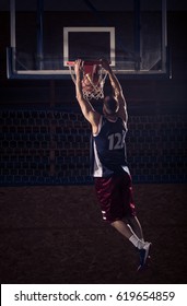 One Young Adult Man, Basketball Player Slam Dunk, In Air. Dark Indoors, Rear View