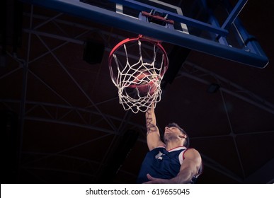 One Young Adult Man, Basketball Player, One Hand, Net Rim, Low Angle View, Slam Dunk, Dark Indoors.