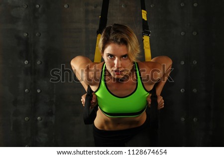 Similar – One young athletic woman at crossfit training, exercising with trx suspension fitness straps over dark background, front view, looking at camera