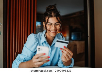 One young beautiful caucasian business woman is buying online on her mobile phone using credit card from her home	 - Powered by Shutterstock