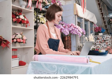 One young Caucasian florist owner works with laptop, website arrangement for online business flora service in colorful flower shop store with beautiful bunch of blossom, e-commerce SME technology. - Powered by Shutterstock