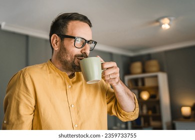 One young caucasian man having cup of coffee while standing at home in sunny day wearing shirt in morning real people copy space - Powered by Shutterstock