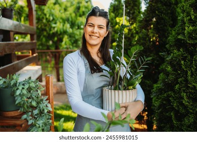 One young caucasian woman is standing proudly holding her potted plant in her garden - Powered by Shutterstock