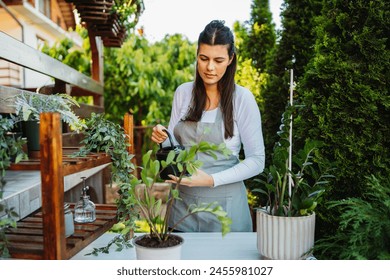 One young caucasian woman is taking care of her plants using plant mister and water can - Powered by Shutterstock