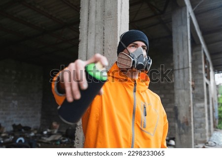 One young guy drawing graffiti on wall with spray can and mask on his face during the day
