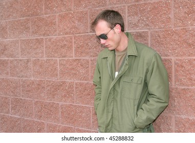 one young guy in a green jacket leaning on the wall looking sad or serious