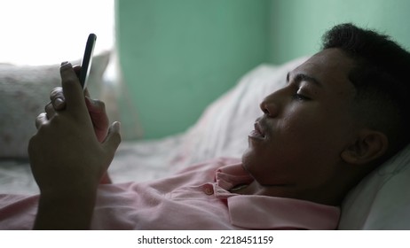 One Young Hispanic Person Browsing Internet On Phone While In Bed Looking At Cellphone Screen