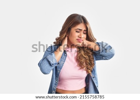 One Young Indian Asian attractive brunette hair woman or female holding a sore neck with hands isolated on a white background screen. Concept of stressed, painful neckache,  hurting muscle spasm