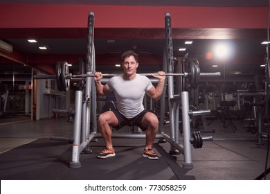 One Young Man, Barbell Back Squat, Dark Gym Indoor. Full Lenght Body Shot.