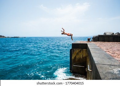 One Young Man Jumping Off A Cliff Doing A Backflip To The Water - Alone Fitness And Healthy Teenager Having Fun Enjoying Alone The Summer And The Sea In His Holiday Vacations