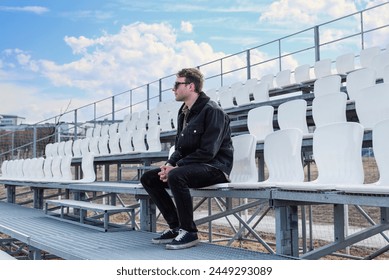 One young man sitting on empty football tribune on the street