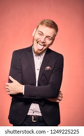 One Young Man, Wearing Suit And Shirt, 20-29 Years Old, Looking To Camera, Candid Smiling Happy, Tongue Out. Real Person, Not Model. Pink Background, Studio Shot, Photo Shoot.