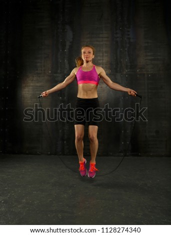 One young middle age athletic, woman training, exercising with fitness jumping rope over dark background, full length front view, looking at camera