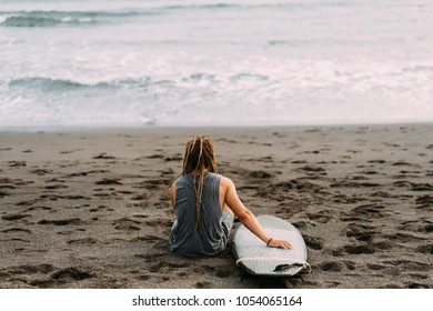 One young surfer man with long dreadlocks sitting near the ocean with his surfboard in Indonesia, Bali, Canggu, Batu Bolong beach. - Powered by Shutterstock