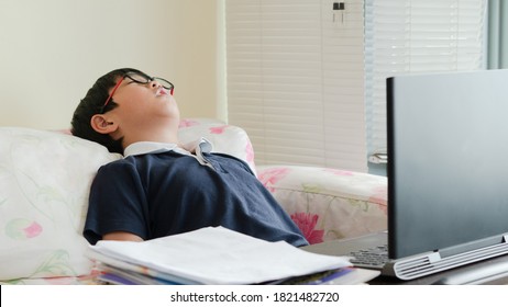 One Young Tired Asian Kid Is Resting Or Taking A Short Nap During His Online Study At Home On The Sofa. Learning From Home With Tiring Concept.