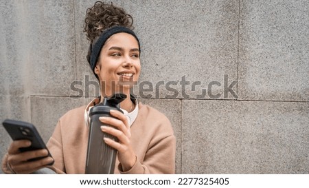 One young woman with headphones hold supplement shaker bottle and smartphone mobile phone sporty caucasian female sit take a brake for training generation z healthy lifestyle concept copy space