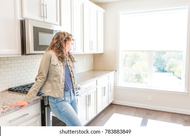 One young woman standing in kitchen in clean, modern, white home design before move-in