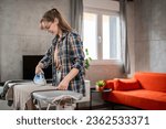 one young woman teenage student ironing clothes at home foo the first time hold iron on shirt on board household chores concept female living in the apartment alone doing housework copy space