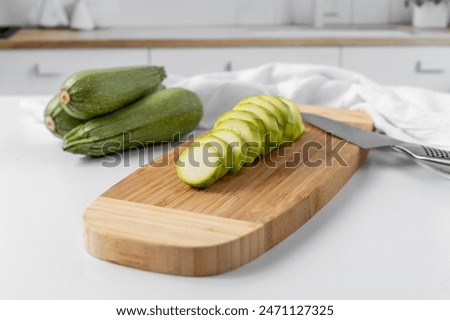 One Zucchini Sliced on a Cutting Board with Three Whole Zucchini in the Background of a Kitchen
