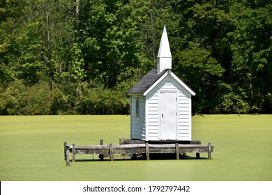 Oneida, New York, USA - August 9, 2020: Cross Island Chapel, the world's smallest church built in 1989, standing in the middle of a pond covered with green scum