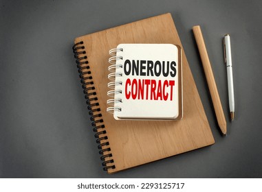 ONEROUS CONTRACT text on a notebook with pen and pencil on grey background