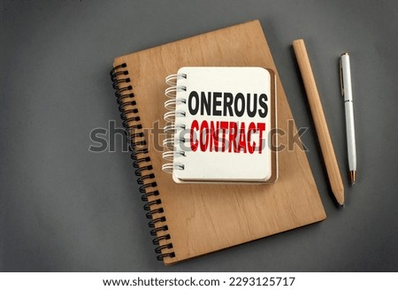ONEROUS CONTRACT text on a notebook with pen and pencil on grey background