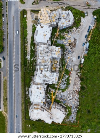 An ongoing construction project shows the floor plans and structure of a future building. Workers and machinery are present, with materials scattered around the site.