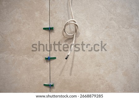 Ongoing renovation and installation work. Green plastic clips securing in place for idyllic alignment. Laying beige color porcelain tiles using wedges and clips. Electrical cord hanging on the wall.