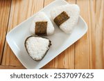 Onigiri made of rice and nori seaweed are spun on a white plate. A simple and delicious Asian snack meal.