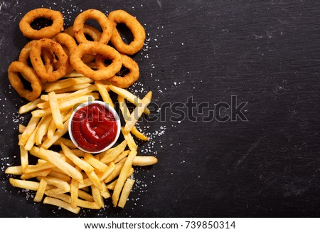 onion rings and french fries with ketchup on dark table, top view