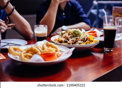 Onion Rings, Nacho Salad And Pint Of Stout (Black Beer) On Wooden Table At The Bar.