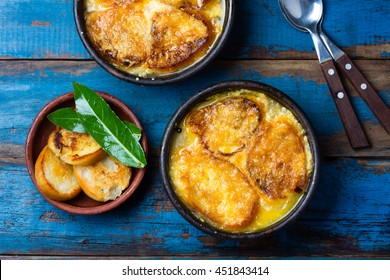 Onion Soup With Dried Bread And Cheese On Clay Bowls On Wooden Blue Background. Top View