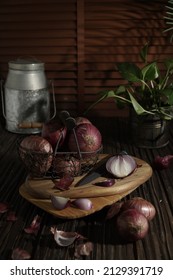 Onion In Wire Black Basket On The Wooden Board. Dark Mood With Blurry Background.