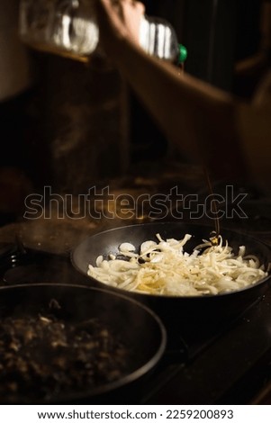 Onions are fried in a pan and drizzled with olive oil. Dark background.