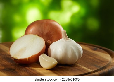 onions and garlic on a cutting board outdoors. a clove of garlic and half an onion along with whole ones on a green background. vegetables ready for cutting close-up. kitchen on a sunny day. - Shutterstock ID 2258601095