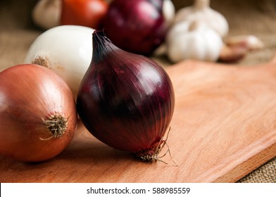 
Onions. Various onions on a board on a background sacking, burlap. Garlic and onion. Violet onions. Garlic. - Powered by Shutterstock