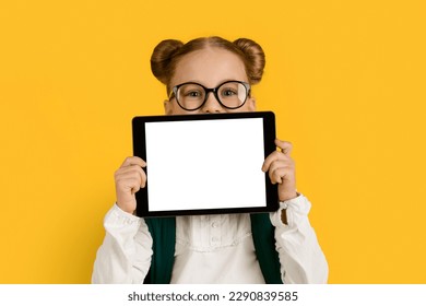 Online Ad. Cute Schoolgirl Holding Blank Digital Tablet With White Screen, Cheerful Preteen Female Kid Advertising New Application Or Website For Study While Posing Over Yellow Background, Mockup - Powered by Shutterstock