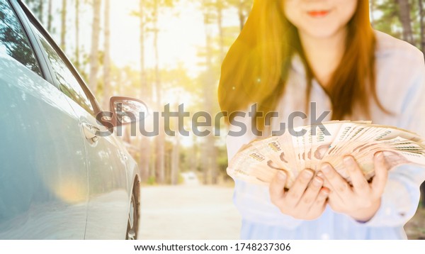 online application\
rent car or insurance support travel activity in new normal from\
lot of money in woman hand with soft focus modern compact car on\
country road background