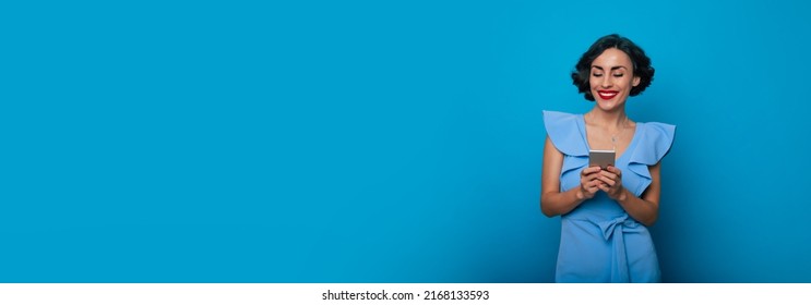 Online. Apps. Typing. Communication. Internet. User. Banner Photo Of Smiling Cute Stylish Brunette Woman With Modern Smart Phone In Hands Isolated On Blue Background