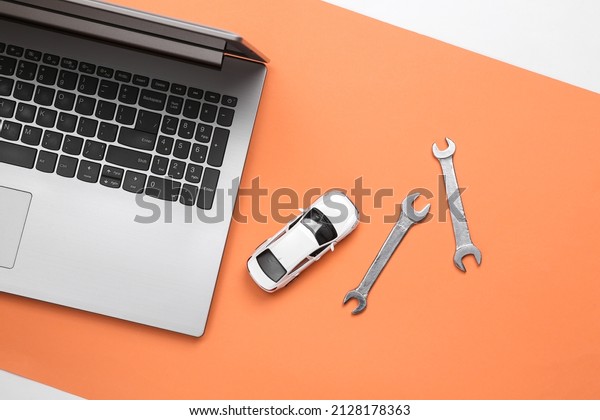 Online auto service. Laptop with toy car and\
wrenches on coral background. Top\
view