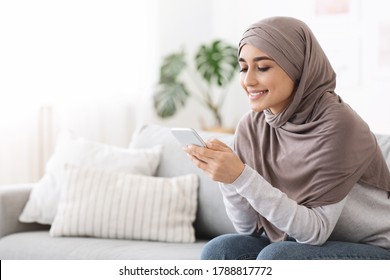 Online Banking. Smiling Muslim Woman In Hijab Using App On Smartphone At Home, Sitting On Couch In Living Room, Copy Space - Powered by Shutterstock