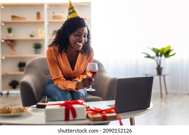 Online Birthday Concept. Black Lady Toasting To Laptop Celebrating B-day Having Video Call Sitting In Front Of Computer And Drinking Wine At Home. Virtual Party, Modern Holiday Celebration