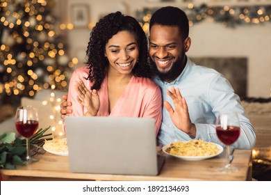 Online Celebration And Communication. Smiling African American Man And Woman Sitting At The Table During Online Video Chat With Friends Or Family Using Laptop, Waving To Webcam, Having Dinner