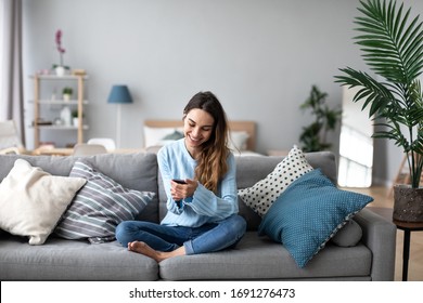  Online-Chat. Lächelnde Frau, die mit Freunden über Smartphone spricht, während sie zu Hause auf dem Sofa sitzt. Porträt eines positiven Mädchens drinnen.