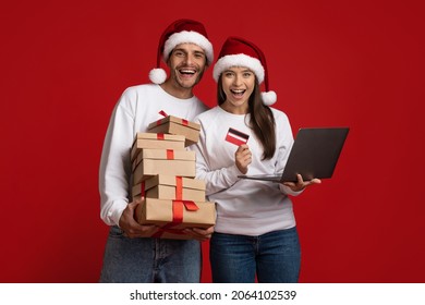 Online Christmas Shopping. Cheerful young couple in santa hats with laptop and credit card buying gifts in internet, excited man and woman enjoying seasonal sales and discounts, red background - Powered by Shutterstock